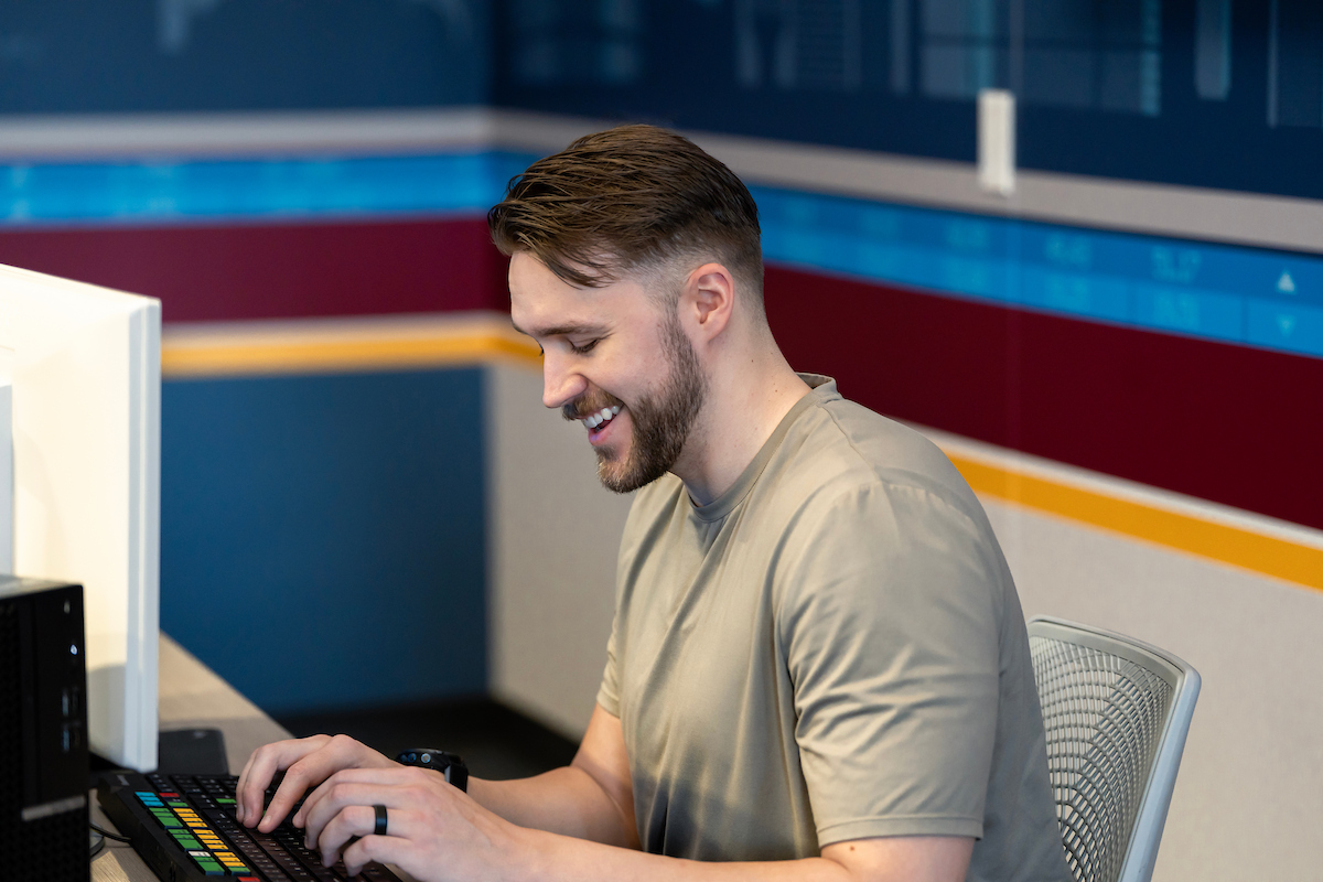 Candid photo of MS-FIN alum Adam Ray smiling and typing on a computer in the W. P. Carey FAR Lab